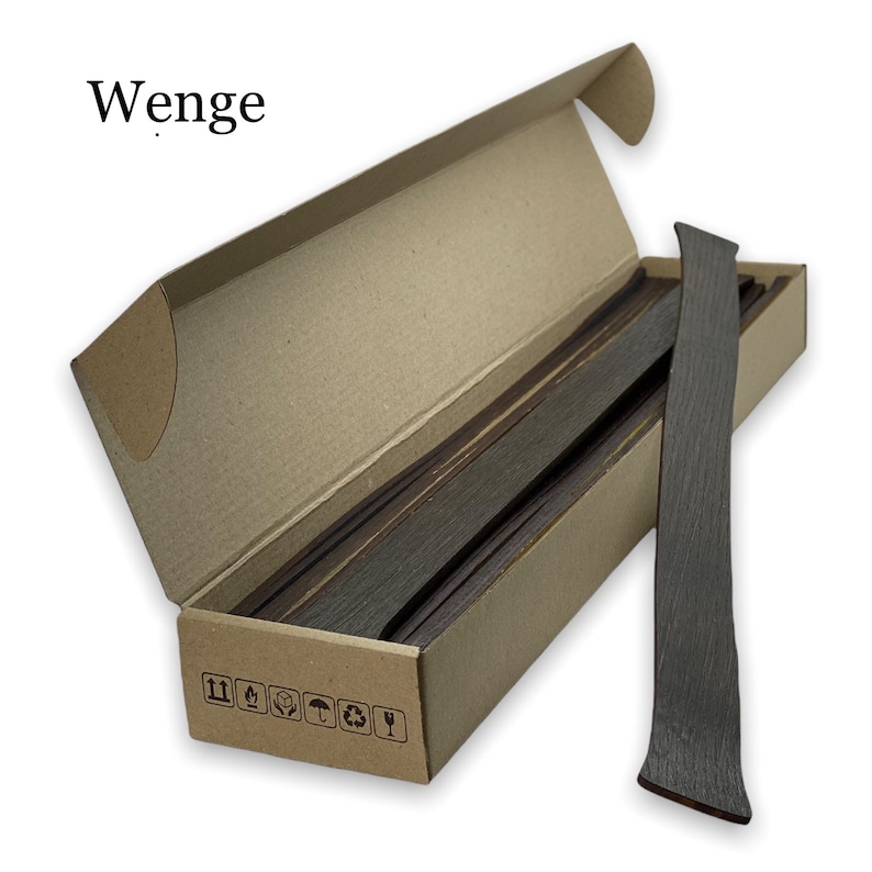 May include: A box of Wenge wood strips, a dark brown wood, in a cardboard box with a brown label. The box is open and the strips are visible. The label has recycling symbols.