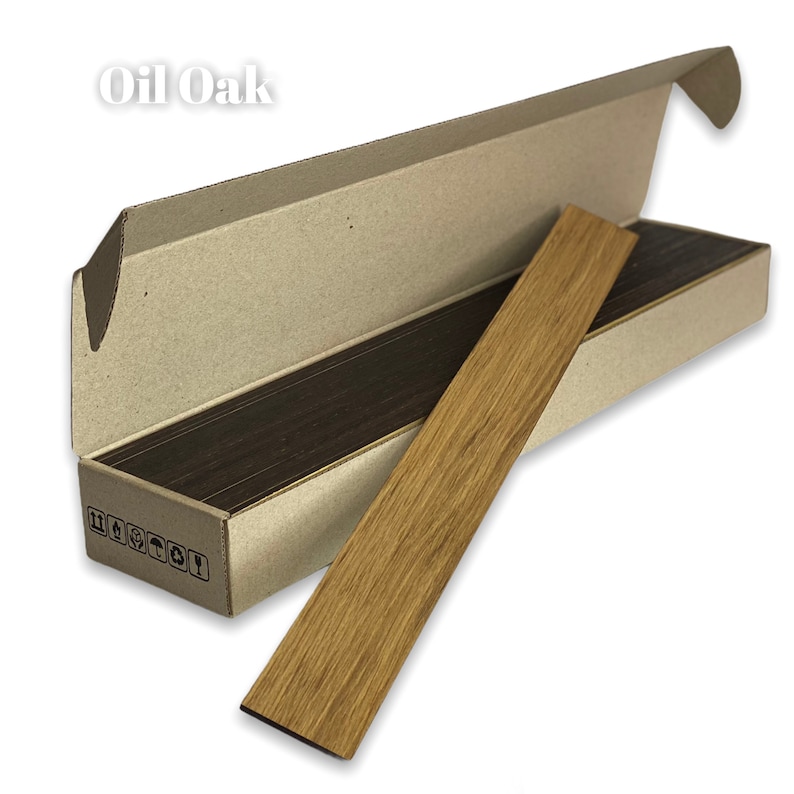 May include: A box of wood veneer sheets in Oil Oak color. The box is open and a single sheet is partially pulled out, showing the wood grain.