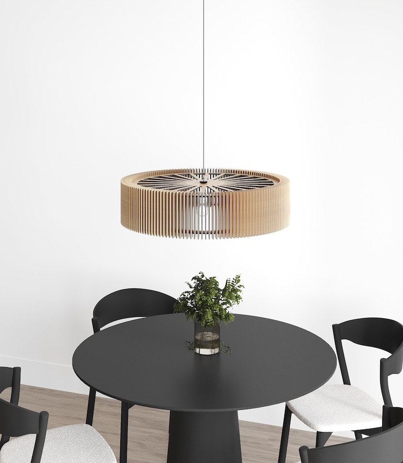 Pu&ograve; includere: Una lampada a sospensione circolare costruita con numerose sottili lamelle di legno chiaro disposte verticalmente in un motivo radiale. La lampada pende da un unico cavo e presenta una fonte luminosa centrale all'interno della struttura.