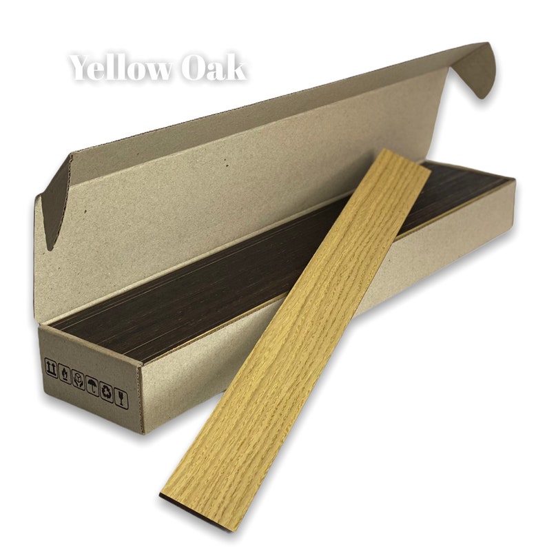 May include: A close-up of a piece of yellow oak wood veneer in a cardboard box. The box is open and the veneer is partially sticking out. The text "Yellow Oak" is printed on the box.