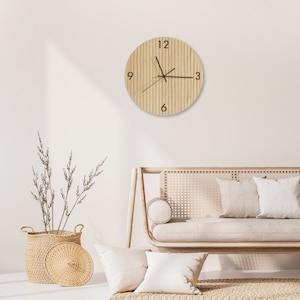 May include: A round wooden wall clock with black hands and numerals at 12, 3, 6, and 9. The clock face has vertical wood grain lines. The clock is hanging on a white wall. The clock's diameter is approximately 12 inches.