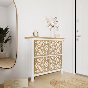 Pode incluir: Um armário branco com quatro portas com um padrão geométrico. O armário tem um tampo de madeira e está colocado num corredor com um espelho, uma porta e um tapete.