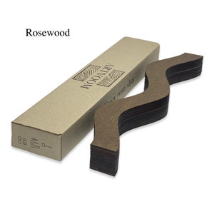 May include: A stack of thin, wavy, rosewood wood slats in a brown cardboard box. The box has the text "ARTWOOD" and "enjoy your slats" printed on it. The wood slats are arranged in a zig-zag pattern.