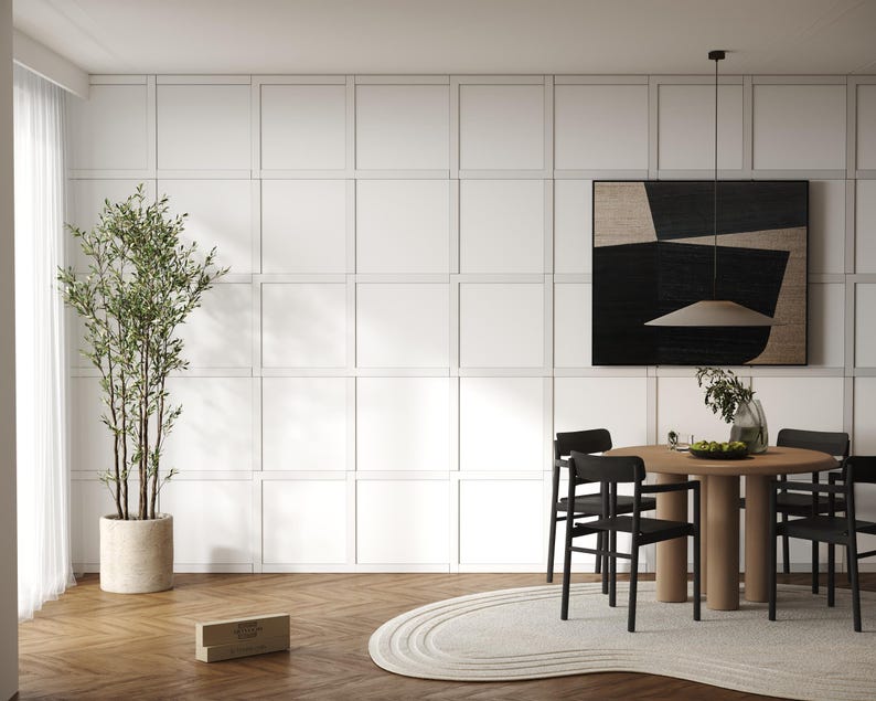 May include: A dining room with a white paneled wall, a black and white abstract painting, a wooden table with black chairs, a potted plant, and a rug.