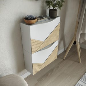 Könnte beinhalten: Ein moderner weißer Schrank mit zwei Schubladen und abgewinkelten Holzakzenten. Der Schrank steht vor einer strukturierten Wand, mit einer kleinen Pflanze und dekorativen Gegenständen oben. Der Boden ist helles Holz.