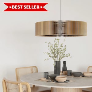 Könnte beinhalten: Eine moderne Pendelleuchte aus Holz mit Lamellendesign hängt über einem Esstisch. Die Leuchte ist kreisförmig und aus hellem Holz gefertigt. Der Tisch ist mit Schalen, Tellern und einer Vase mit Grünzeug gedeckt. Das Bild enthält ein "BEST SELLER" Banner.