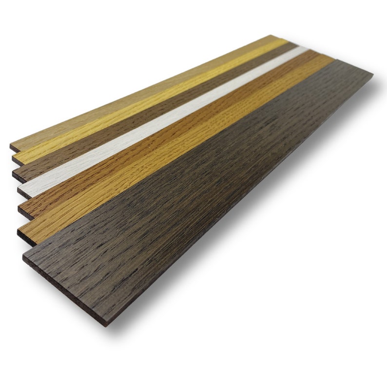 May include: A stack of six rectangular wooden veneer strips arranged in a fan pattern. The strips display a variety of wood grain finishes, ranging from light natural oak and golden tones to a stark white, medium brown, and a deep dark espresso.