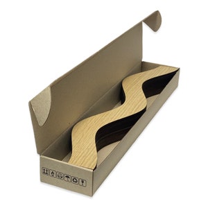 May include: A cardboard box with a wavy wooden piece inside. The box is open and the wooden piece is visible. The box has recycling symbols printed on the bottom.