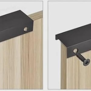 Op de afbeelding: Een matzwarte rechthoekige randgreep gemonteerd op een lichtgekleurde kastdeur met houtnerf. De greep heeft een plat bovenoppervlak en een naar beneden gerichte lip. Twee zwarte schroeven zijn door de greep in de kastdeur gestoken.