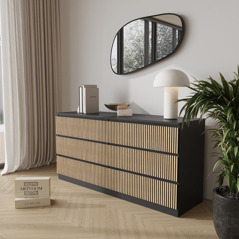 May include: A modern black dresser with three rows of vertical, light-colored wood slats. The dresser is in a room with a large mirror, a white lamp, and a potted plant. Two boxes with the text "ARTVOOM" are on the floor.