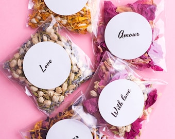 May include: Five small clear plastic bags filled with dried flower petals. Each bag has a white circle sticker with black text. The text on the stickers reads "Forever", "Amour", "Love", "With love", and "Amour".