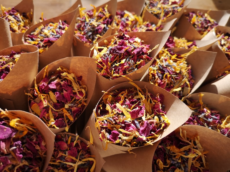 Puede incluir: Conos de papel marr&oacute;n llenos de p&eacute;talos de flores secas en tonos de amarillo, rosa y morado. Los p&eacute;talos son una mezcla de rosa, lavanda y otras flores.