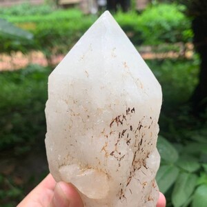 以下が含まれることがあります： 茶色のインクルージョンが入った大きな透明な水晶。水晶はピラミッド型で、表面は滑らかで磨かれています。
