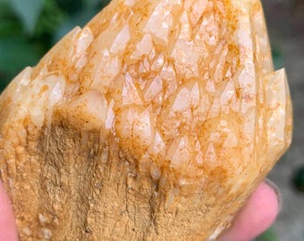 May include: A raw, golden-orange quartz crystal cluster featuring a textured, matte base that transitions into translucent, faceted points. The surface displays natural iron staining with warm amber hues across the crystalline structure.