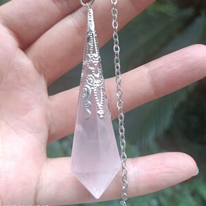 May include: A pink quartz crystal pendulum with a silver chain and ornate metal accents. The pendulum is hanging from a silver clasp.