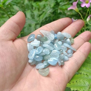Op de afbeelding: Een handvol lichtblauwe, getrommelde aquamarijnstenen. De stenen zijn glad en gepolijst en hebben verschillende vormen en maten.