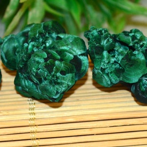 May include: Four green malachite stones with a banded pattern. The stones are smooth and have a natural, organic shape.