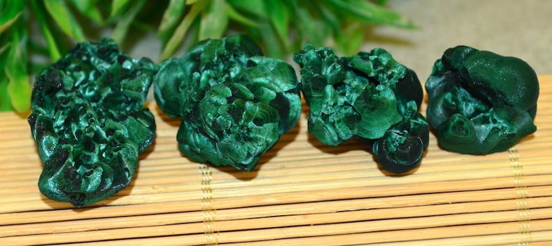 May include: Four green malachite stones with a banded pattern. The stones are smooth and have a natural, organic shape.