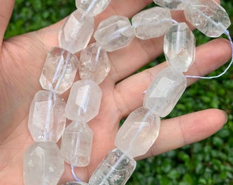 May include: A strand of clear, faceted quartz beads with a polished finish. Each bead features a multi-sided, irregular geometric shape and is strung together on a thin, light-colored cord, showcasing natural internal inclusions and transparency.