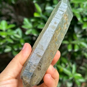 May include: A clear, faceted quartz crystal with a grey hue and inclusions. The crystal is pointed at both ends and has a natural, rough texture.