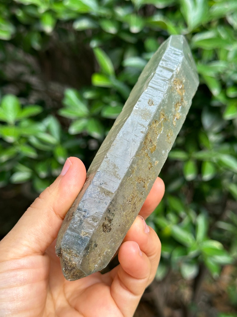 May include: A clear, faceted quartz crystal with a grey hue and inclusions. The crystal is pointed at both ends and has a natural, rough texture.