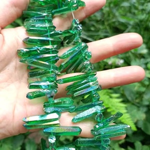 May include: A strand of green iridescent crystal points, also known as aura quartz, strung together for jewellery making. The crystals are faceted and have a shimmery, rainbow-like effect.