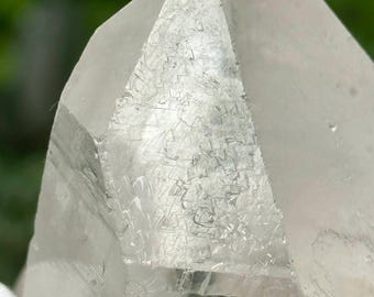 May include: A clear quartz crystal with a pointed tip and a faceted surface. The crystal has a natural, rough texture and is translucent.