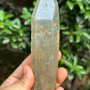 May include: A large, clear, green quartz crystal point with a rough, natural finish. The crystal is approximately 15 cm long and has a hexagonal shape.
