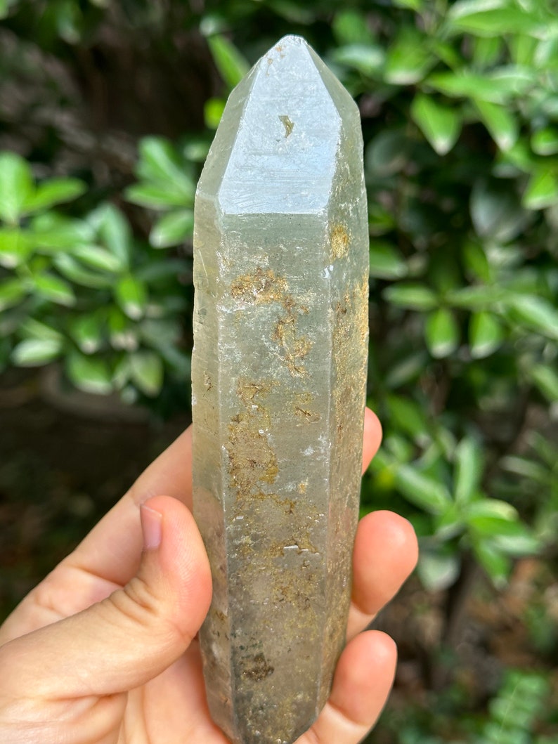 May include: A large, clear, green quartz crystal point with a rough, natural finish. The crystal is approximately 15 cm long and has a hexagonal shape.