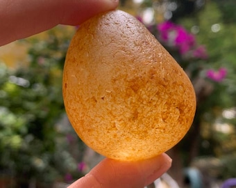 May include: A smooth, teardrop-shaped, amber-colored stone with a translucent, slightly cloudy appearance.