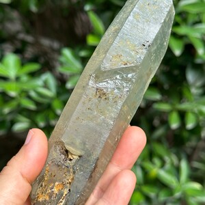 May include: A large, clear quartz crystal with a green hue and brown inclusions. The crystal is pointed at both ends and has a rough, natural texture.
