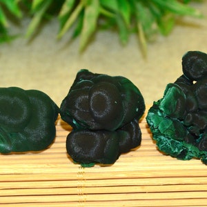 May include: Three green malachite mineral specimens with a smooth, rounded surface. The specimens are arranged in a row on a bamboo mat.
