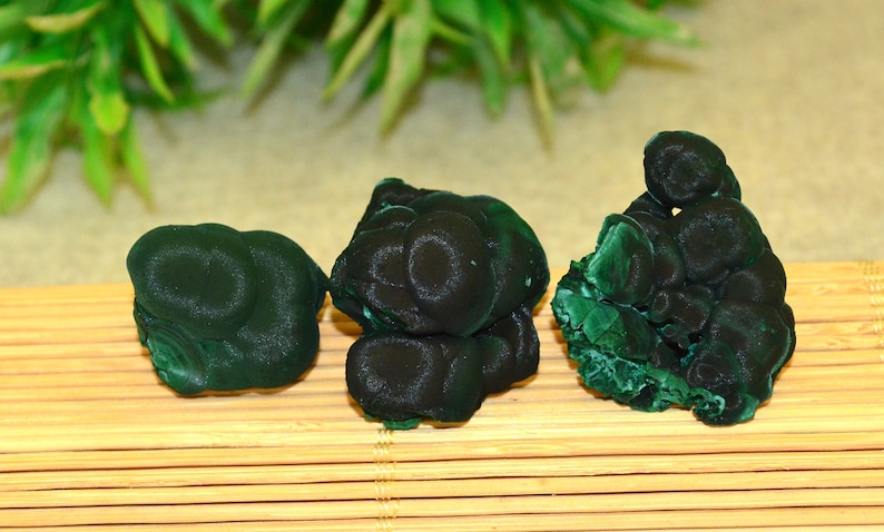 May include: Three green malachite mineral specimens with a smooth, rounded surface. The specimens are arranged in a row on a bamboo mat.