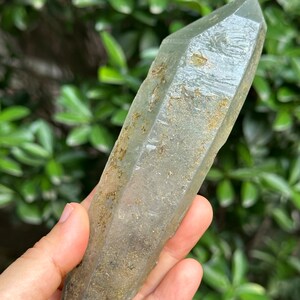 May include: A large, clear quartz crystal with a green hue and brown inclusions. The crystal is pointed at both ends and has a rough, natural texture.