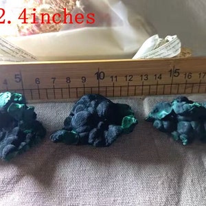 May include: Three green and black malachite mineral specimens, each measuring approximately 2-2.4 inches in length, are displayed on a wooden ruler with markings from 1 to 20.