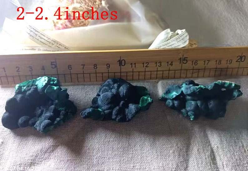May include: Three green and black malachite mineral specimens, each measuring approximately 2-2.4 inches in length, are displayed on a wooden ruler with markings from 1 to 20.