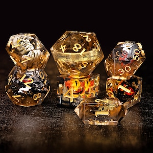 Op de afbeelding: Een verzameling heldere, veelzijdige dobbelstenen met gouden cijfers en ingebedde miniatuurfiguren. De dobbelstenen hebben een goud- en amberkleurenschema, met rode en zwarte accenten. De dobbelstenen zijn ontworpen voor tabletop gaming.