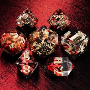 May include: A set of seven polyhedral dice made of clear resin with embedded red and black swirling patterns and gold-colored numbers. The collection includes a d20, d12, d10, d8, d6, d4, and a percentile die, all featuring sharp edges and distinct numerical faces.