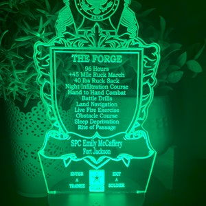 May include: Green illuminated acrylic sign with a US Army emblem, a shield with the text "THE FORGE" and a list of training exercises, including a 45-mile ruck march, 40 lbs ruck sack, night infiltration course, hand-to-hand combat, battle drills, land navigation, live fire exercise, obstacle course, sleep deprivation, and rite of passage. The sign also includes the text "SPC Emily McCaffery, Fort Jackson".