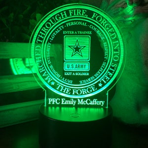 May include: A green LED night light with a circular design featuring the words "Through Fire, Forged Into Steel" and the U.S. Army logo. The text "PFC Emily McCaffery" is displayed below the logo.