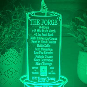 May include: A green illuminated sign shaped like a candle with the text "THE FORGE" and details about a military training exercise. The text includes "96 Hours", "45 Mile Ruck March", "40 lbs Ruck Sack", "Night Infiltration Course", "Hand to Hand Combat", "Battle Drills", "Land Navigation", "Live Fire Exercise", "Obstacle Course", "Sleep Deprivation", "Rite of Passage", "ENTER A TRAINEE", "EXIT A SOLDIER", "PFC Tanner Young", "Fort Sill, OK", and "February 17-19, 2025".