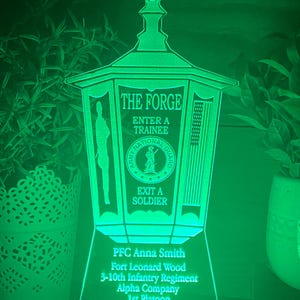 May include: A green illuminated lantern with the text "The Forge" and "Enter a Trainee" and "Exit a Soldier". The lantern also has the text "Army National Guard" and a graphic of a soldier. The lantern has a personalized inscription that reads "PFC Anna Smith, Fort Leonard Wood, 3-10th Infantry Regiment, Alpha Company, 1st Platoon".