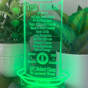 May include: A green acrylic candle with the text "THE FORGE" and a list of challenges including "96 Hours", "45 Mile Ruck March", "40 lbs Ruck Sack", "Night Infiltration Course", "Hand to Hand Combat", "Battle Drills", "Land Navigation", "Live Fire Exercise", "Obstacle Course", "Sleep Deprivation", "Rite of Passage", "ENTER A TRAINEE", "EXIT A SOLDIER", "SPC Robert Olson", "Ft Leonard Wood", and "May 7-9, 2022".