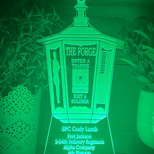 May include: A green illuminated acrylic sign with the text "The Forge" and "Enter a Trainee" and "Exit a Soldier". The sign also includes a silhouette of a soldier, a star, and a US Army logo. The bottom of the sign has the text "SPC Cody Lamb, Fort Jackson, 3-34th Infantry Regiment, Alpha Company, 4th Platoon".