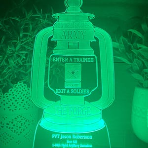 May include: A green illuminated acrylic plaque with a lantern design. The lantern has the text "United States Army", "Enter a Trainee", "Exit a Soldier", and "The Forge". The plaque also has the text "PVT Jason Robertson", "Fort Sill", "1-40th Field Artillery Battalion", "Bravo Battery", and "3rd Platoon".