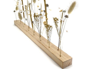 Può includere: Un blocco di legno con più fori per fiori secchi. Il blocco è in legno chiaro e ha una finitura naturale. I fiori sono di vari colori e trame, tra cui bianco, marrone e beige.