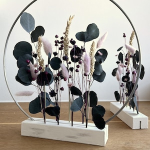 Peut inclure: Arrangement florale séchée dans une base en bois blanc avec un cerceau en métal. L'arrangement comprend des fleurs séchées roses et bordeaux, des feuilles d'eucalyptus et des épis de blé.
