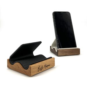 Könnte beinhalten: Handyhalter aus Holz mit schwarzer Filzwiege. Ein Ständer hat ein Telefon darin. Der andere Ständer hat den Text "Beste Mama" eingraviert. Die Ständer sind aus hellbraunem Holz.