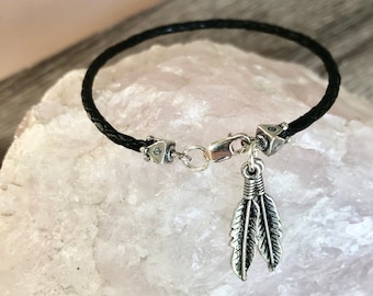 Pulsera con dije de cuero trenzado negro, detalles de plata de ley y dije de pluma.