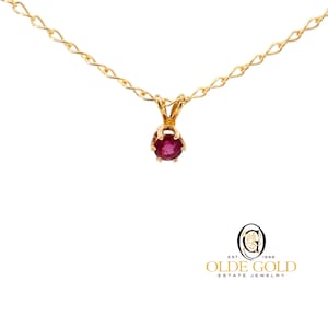 May include: A gold chain necklace with a small ruby pendant. The ruby is set in a gold crown-like setting.